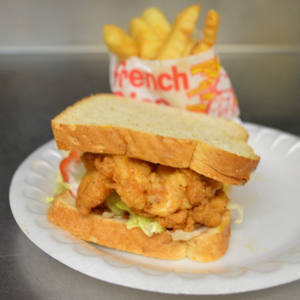 Fried shrimp sandwich on white bread with lettuce, tomato, and a side of French fries.