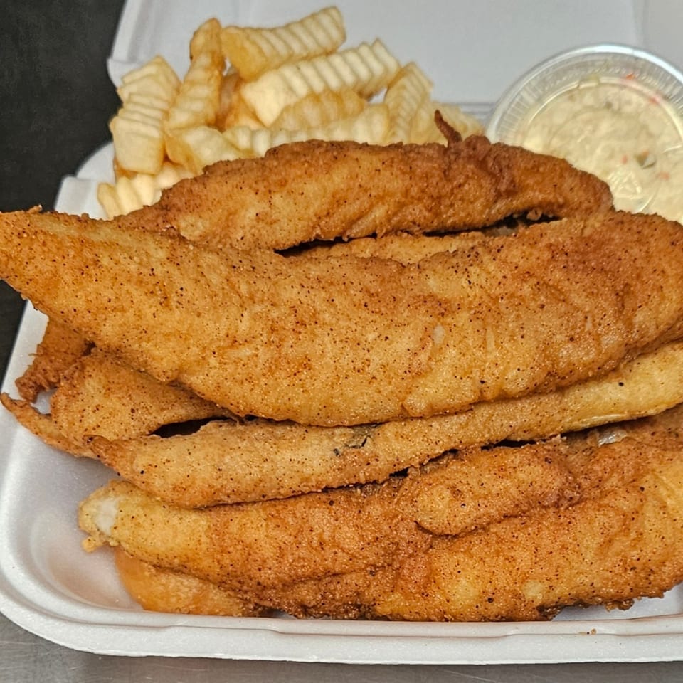 Golden-brown fried fish fillets with crinkle-cut fries and tartar sauce in a white takeout container.