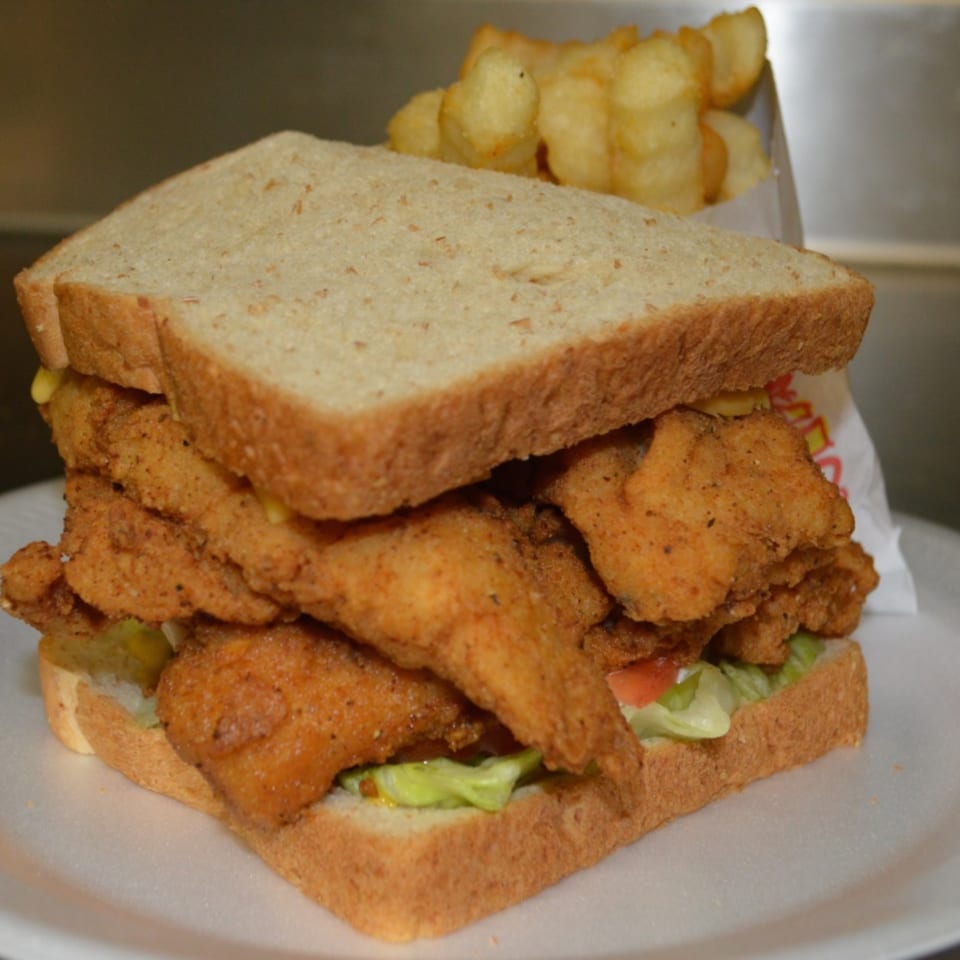 A fried fish sandwich on wheat bread with lettuce and tomato, served with a side of fries.