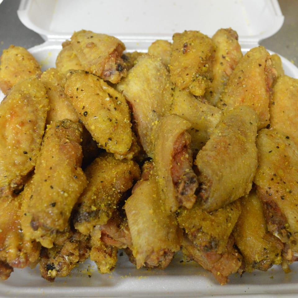 A white takeout container overflowing with golden-brown, seasoned chicken wings.