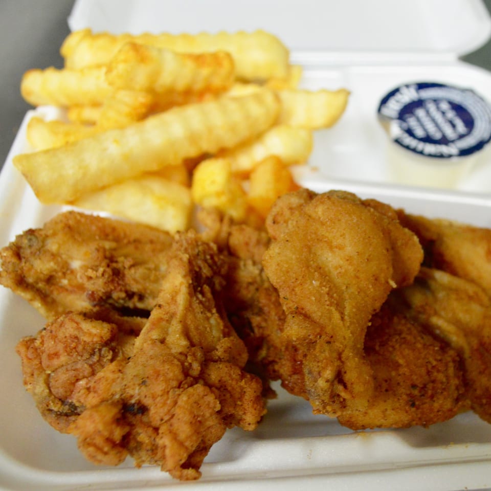 Crispy fried chicken wings and crinkle-cut fries in a white takeout container with a sauce cup.