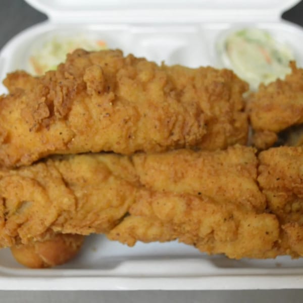 Crispy fried fish fillets and hush puppies with coleslaw in a white takeout container.