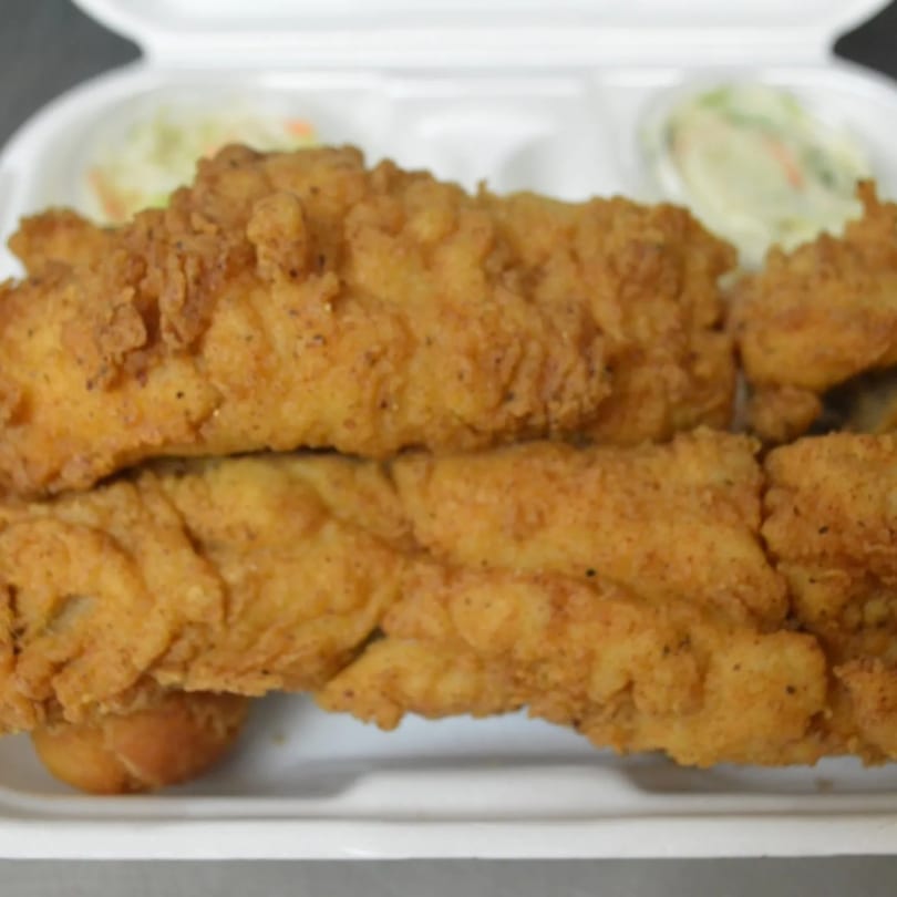 Crispy fried fish fillets and hush puppies with coleslaw in a white takeout container.