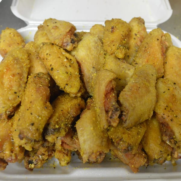 A white takeout container filled with golden-brown, seasoned chicken wings, ready to eat.