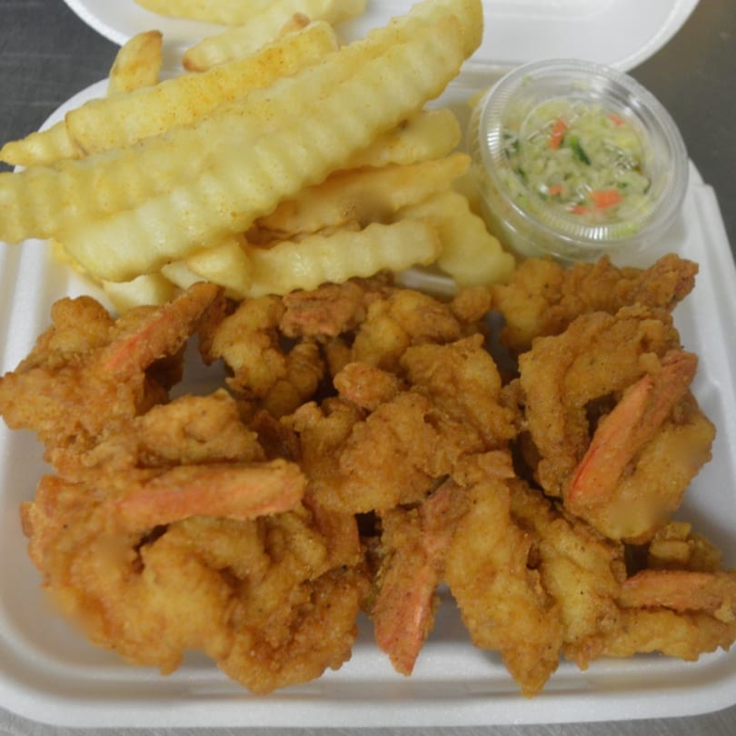 Fried shrimp and crinkle-cut fries with a side of coleslaw in a white takeout container.
